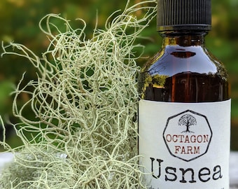 May include: A brown glass bottle with a dropper top, labeled "Octagon Farm Usnea double extraction tincture 2 fl oz crafted in Fletcher, VT". The bottle is sitting on a wooden surface next to a clump of light green lichen.