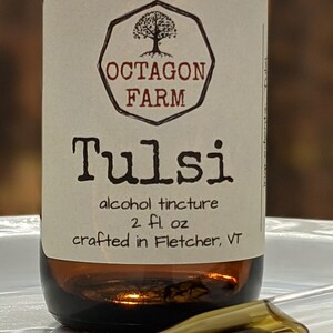 May include: A brown glass bottle with a white label that reads "Octagon Farm Tulsi alcohol tincture 2 fl oz crafted in Fletcher, VT". The label features a black and white illustration of a tree in an octagon.