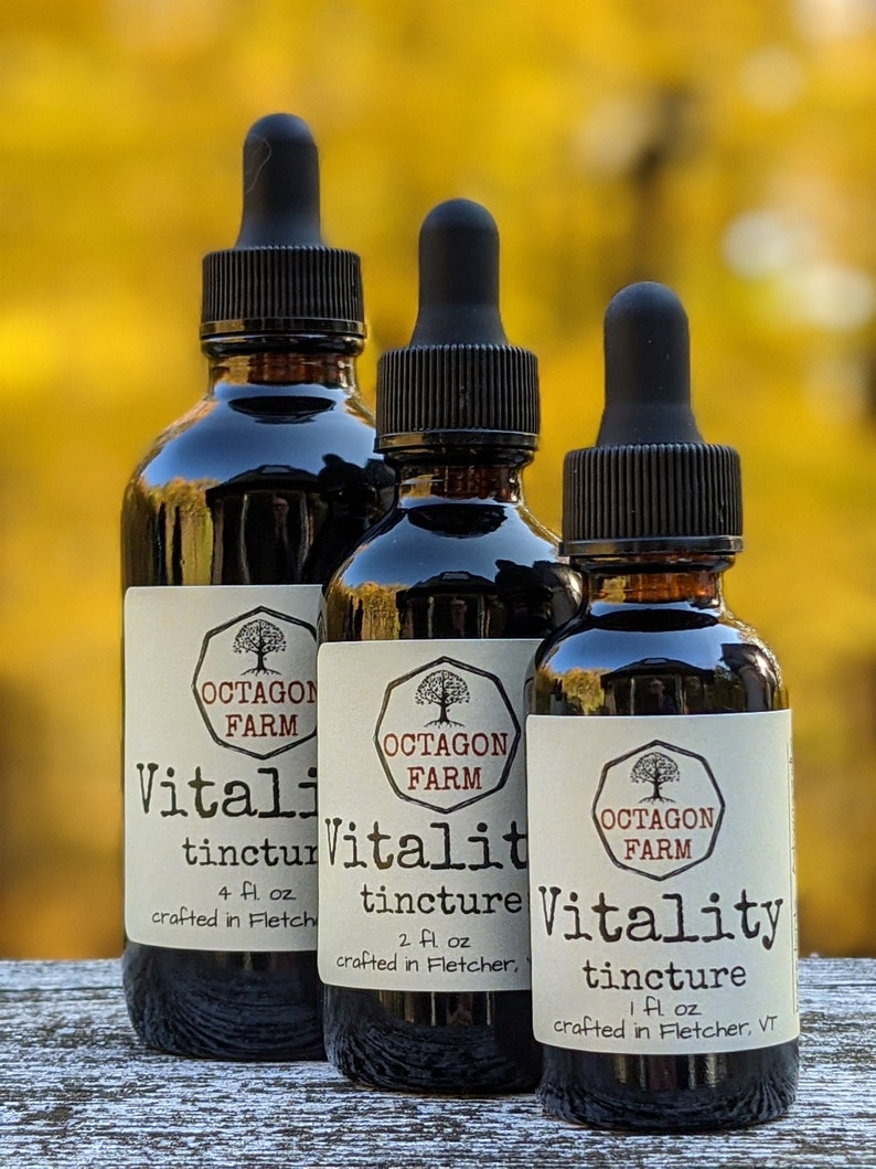 Puede incluir: Tres botellas de vidrio con goteros, etiquetadas "Vitality tincture" de "Octagon Farm". Las botellas est&aacute;n llenas de un l&iacute;quido oscuro y est&aacute;n dispuestas en una fila sobre una superficie de madera. Las botellas est&aacute;n etiquetadas con diferentes tama&ntilde;os: 4 fl oz, 2 fl oz y 1 fl oz.