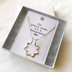 May include: A silver necklace with a gold flower pendant in a white box. The box has a card inside that reads "for pete's sake... it's a keepsake."
