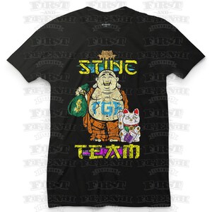 May include: Black t-shirt with a graphic of a cartoon Buddha holding a bag of money and a lucky cat. The text "STING PG" and "T-TEAM" are printed on the shirt.
