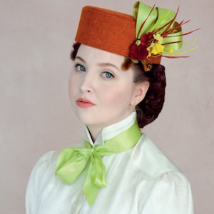 May include: A woman wearing a white blouse with a green bow tie and a brown hat with a floral embellishment.