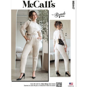 May include: Sewing pattern for a two-piece outfit, featuring a cropped top and pants. The outfit is in a light beige color and is shown on two models. The pattern is from McCall's and is called "Brandı Joan" with the number M8447.