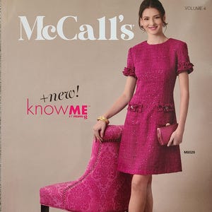 May include: A McCall's sewing pattern cover featuring a woman in a fuchsia dress. The dress has short sleeves and decorative pockets. The woman is holding a matching clutch and is standing next to a pink patterned chair. The text "McCall's" and "knowME" are visible.