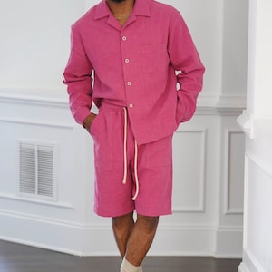 May include: A pink linen shirt and matching shorts set. The shirt has a collared neckline and long sleeves. The shorts have a drawstring waist and pockets. The person is wearing white sneakers and socks.