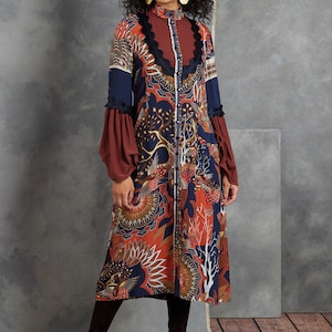 Può includere: Un abito a maniche lunghe con una stampa floreale colorata e un collo a balze. L'abito ha una chiusura con bottoni sul davanti e maniche lunghe con balze ai polsini. L'abito è realizzato in un tessuto leggero e ha una vestibilità rilassata.