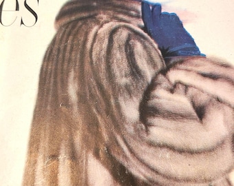 May include: A woman wearing a long, gray fur coat with a blue hat and gloves. The hat has a blue feather on top. The woman is looking over her shoulder.
