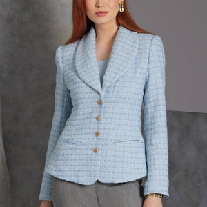 Puede incluir: Blazer de tweed azul claro con botones dorados. El blazer tiene un cuello clásico y un corte entallado. La modelo lleva pantalones grises y pendientes dorados. El blazer es una adición elegante a cualquier guardarropa.