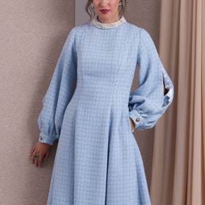May include: A light blue dress with a high neckline and long sleeves. The dress has a fitted bodice and a flared skirt. The sleeves are puffed at the shoulders and have a satin lining. The dress has a pearl trim at the neckline.