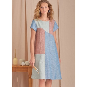 Può includere: Una donna indossa un vestito a maniche corte con un motivo geometrico in tonalità di blu, verde e rosa. Il vestito ha una vestibilità rilassata e una silhouette leggermente a trapezio.