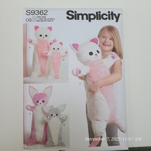 Puede incluir: Patrón de costura Simplicity S9362 con diseños de animales de peluche. El patrón incluye un gran juguete de peluche con forma de gato blanco y rosa, junto con versiones más pequeñas y otros diseños de animales. La imagen muestra a un niño sosteniendo el peluche de gato.