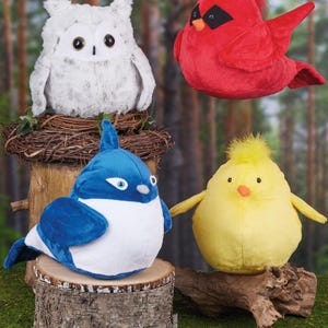 May include: Four plush bird toys: a white owl in a nest, a red cardinal, a blue bird, and a yellow chick. The toys are on a wooden surface with a forest background.