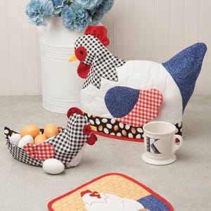 May include: A collection of farmhouse-style kitchen decor featuring a chicken theme. Includes a quilted chicken-shaped egg basket, a chicken-shaped tea cozy, a mug with the letter "K", and a matching pot holder. The items feature red, black, white, and blue patterns.
