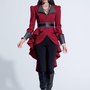 Peut inclure: Veste bordeaux à col montant et ceinture noire. La veste a un design péplum et est associée à un pantalon noir et à de hautes bottes noires. Les manches ont des poignets gris avec une bordure en dentelle blanche.