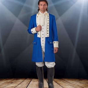Puede incluir: Una capa de disfraz azul y blanca con botones plateados y puños blancos. La capa es larga y tiene un cuello alto. La persona que lleva la capa está de pie sobre un suelo de madera.