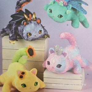 以下が含まれることがあります： 様々な装飾が施された、猫のようなぬいぐるみたちのコレクション。紫色の翼と角を持つもの、花のアクセントが付いた緑色のもの、ひまわりが付いた黄色いもの、王冠が付いたピンク色のものがあります。それぞれ大きな目を持っています。