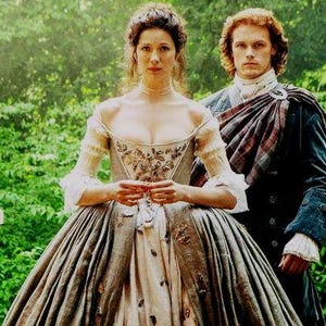 May include: A couple in a woodland setting. The woman is wearing a long, flowing, light blue and white dress with a floral pattern. The man is wearing a traditional Scottish kilt with a tartan pattern.