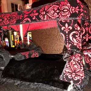 Puede incluir: Una cama con dosel en miniatura negra y roja con un patrón floral decorativo. El marco de la cama es negro con detalles en rojo, y el dosel está adornado con lazos negros. La cama es probablemente para una muñeca u otra figura pequeña.