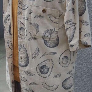 May include: A beige button-up shirt with a black and white avocado print. The shirt has a pocket on the left chest and short sleeves.