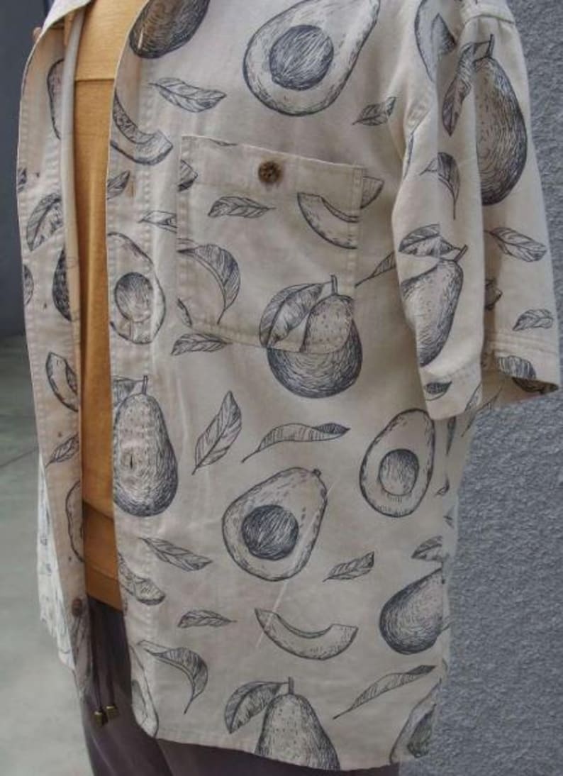 May include: A beige button-up shirt with a black and white avocado print. The shirt has a pocket on the left chest and short sleeves.
