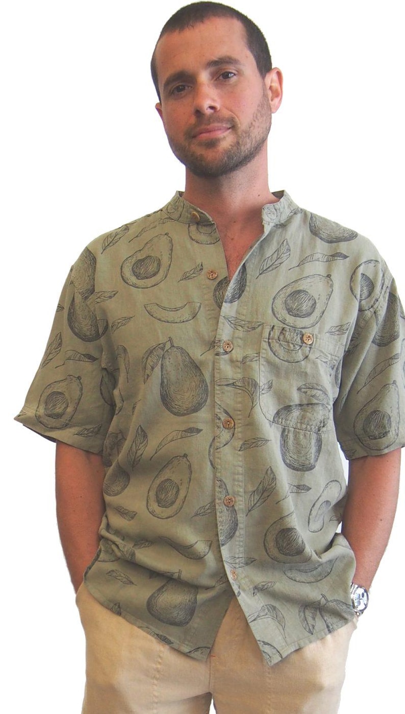 May include: A man wearing a green short-sleeved shirt with a black and white avocado print. The shirt has a mandarin collar and a button-up front.