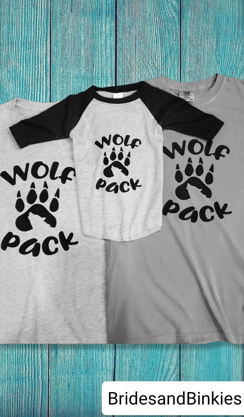 Puede incluir: Tres camisetas grises con letras negras y un gr&aacute;fico de huella de pata. Las camisetas dicen "Wolf Pack".