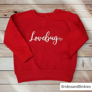 May include: Red sweatshirt with the text "Lovebug" in white cursive lettering with a small heart symbol.