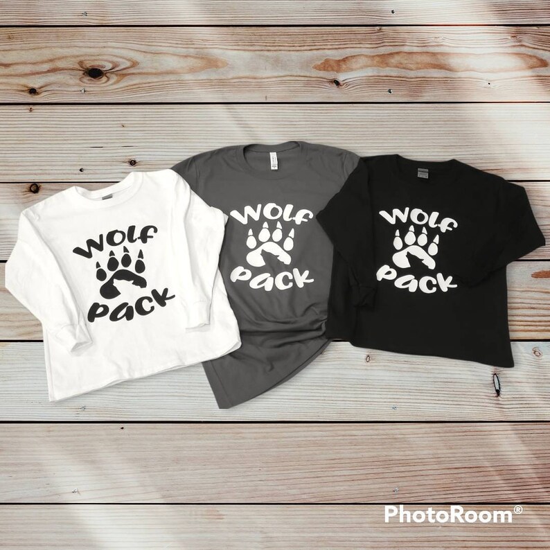 Puede incluir: Tres camisas de manga larga con el texto "Wolf Pack" y un dise&ntilde;o de huella de pata. Las camisas son blancas, grises y negras.