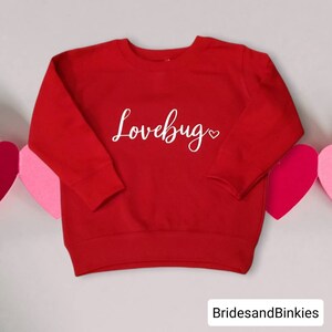 May include: Red long-sleeved sweatshirt with the text "Lovebug" in white cursive lettering with a small heart.