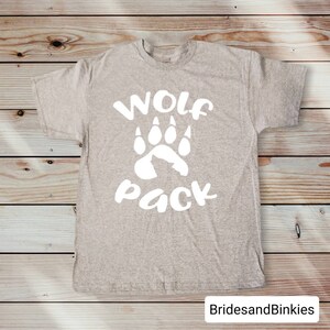 Puede incluir: Una camiseta gris con una huella de pata de lobo blanca y el texto "Wolf Pack" impreso en la parte delantera.