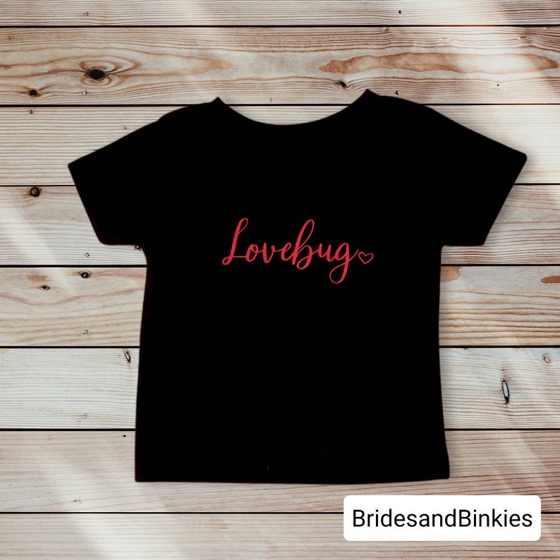 May include: Black t-shirt with the text "Lovebug" in red cursive lettering with a small red heart.