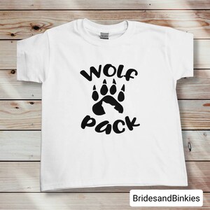 Puede incluir: Camiseta blanca con una huella de pata de lobo negra y el texto "Wolf Pack" impreso en la parte delantera.