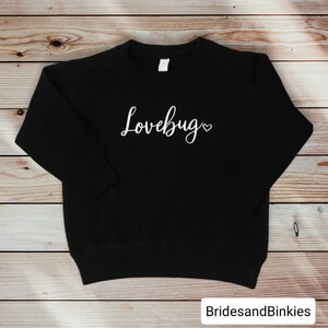 May include: Black sweatshirt with the text "Lovebug" in white cursive lettering with a small heart symbol.