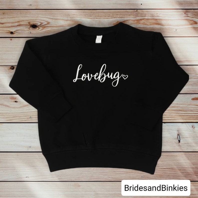 May include: Black sweatshirt with the text "Lovebug" in white cursive lettering with a small heart symbol.