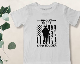 May include: White t-shirt with a black graphic of a soldier standing in front of an American flag. The text "Proud Niece of a US Army Soldier" is printed on the shirt.
