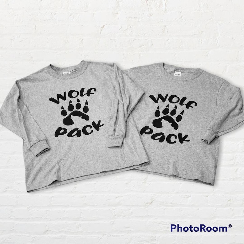 Puede incluir: Dos camisas grises de manga larga con el texto "Wolf Pack" y un gr&aacute;fico de huella de lobo negro.