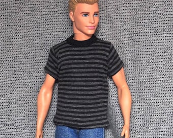 May include: A doll wearing a black and gray striped t-shirt and blue jeans.