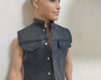 May include: A black leather vest with a snap closure and a denim-style pocket on the front. The vest is worn by a doll with blonde hair and blue eyes.
