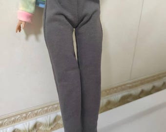 Könnte beinhalten: Graue Jogginghose für eine Puppe. Die Hose ist aus weichem, dehnbarem Stoff und hat eine bequeme Passform.
