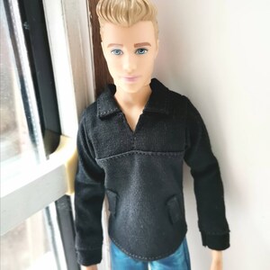 May include: A doll with blond hair wearing a black long-sleeved shirt and blue jeans.