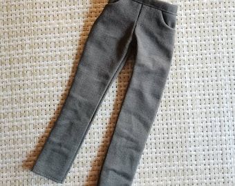 Könnte beinhalten: Graue Puppen-Hose mit Cordstruktur. Die Hose hat ein figurbetontes Design mit einer kleinen Tasche auf der rechten Seite. Die Hose ist aus weichem Stoff und für eine Puppe geeignet.
