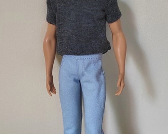 May include: A doll wearing a gray t-shirt and light blue pants. The doll has short brown hair and is wearing white sneakers.