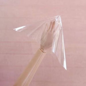 May include: A clear plastic sheet held up by a hand, the sheet is shaped like a cone.