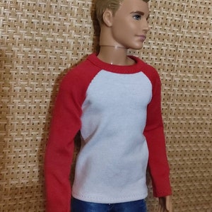 May include: A doll wearing a white long-sleeved shirt with red sleeves and blue jeans.