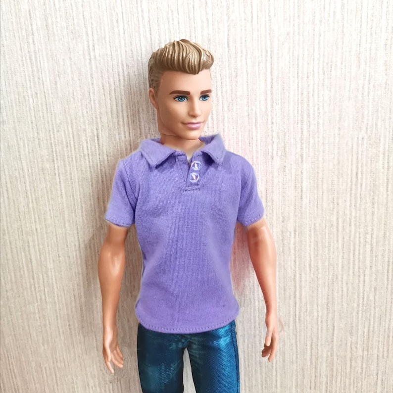 Puede incluir: Una mu&ntilde;eca con una camisa polo morada y pantalones vaqueros azules.