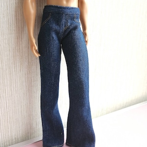 May include: Dark blue denim doll pants with a flared leg design. The pants have yellow stitching details and a classic five-pocket style. The doll pants are made of a textured denim fabric.
