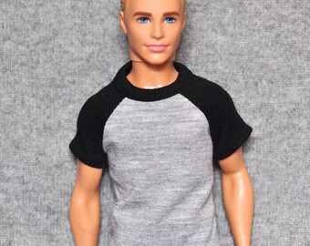 May include: A gray and black t-shirt with a baseball style design. The shirt has short sleeves and a crew neck.
