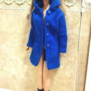 May include: A blue hooded coat with buttons and pockets, worn by a doll with blonde hair and black boots.