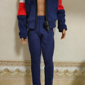 May include: A blue tracksuit with a zipped jacket and matching trousers. The jacket has white and red colour blocking on the sleeves.