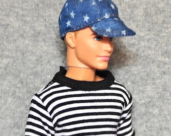 Puede incluir: Una muñeca con una camisa a rayas blancas y negras y una gorra de béisbol de mezclilla azul con estrellas blancas.